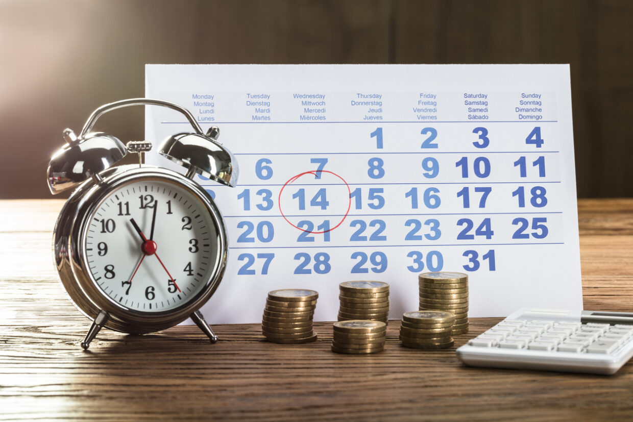 Payment Time On Alarm Clock With Coins, Calculator And Calendar Over The Wooden Table