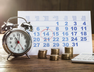 Payment Time On Alarm Clock With Coins, Calculator And Calendar Over The Wooden Table