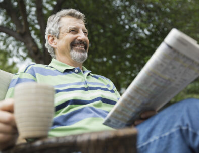 Happy senior man with coffee cup and newspaper sitting in yard