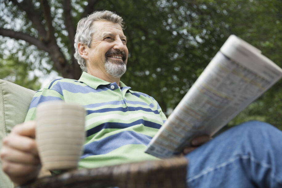 Happy senior man with coffee cup and newspaper sitting in yard